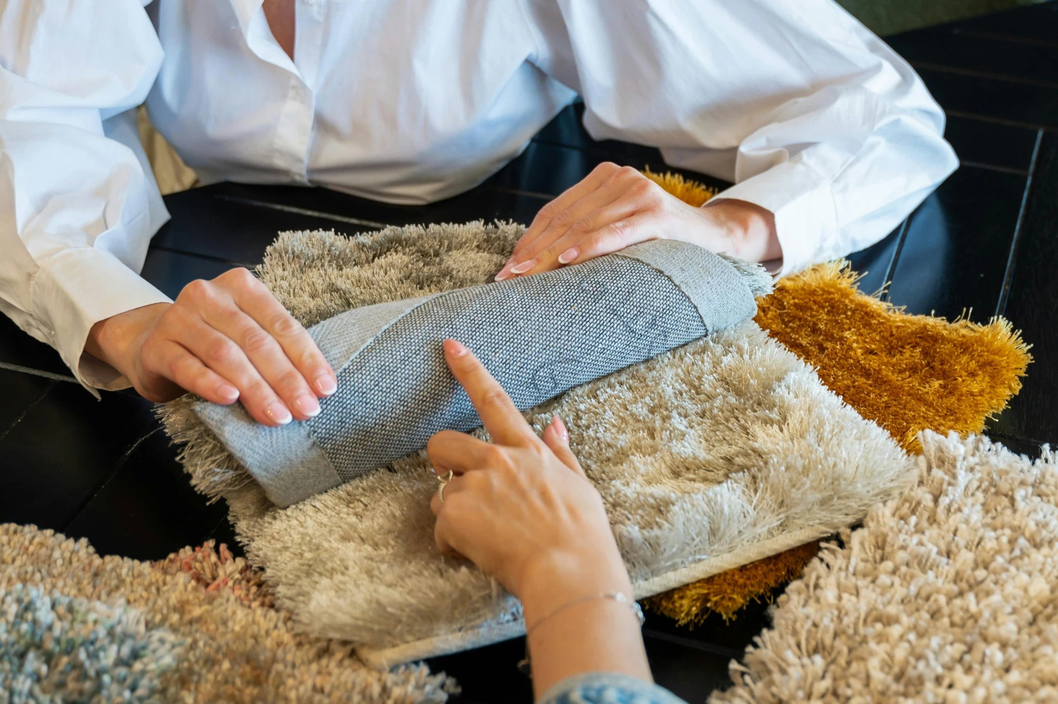 Close-up of a Volero adviser and a customer feeling the pile of a rolled rug sample above stacked shaggy rug swatches