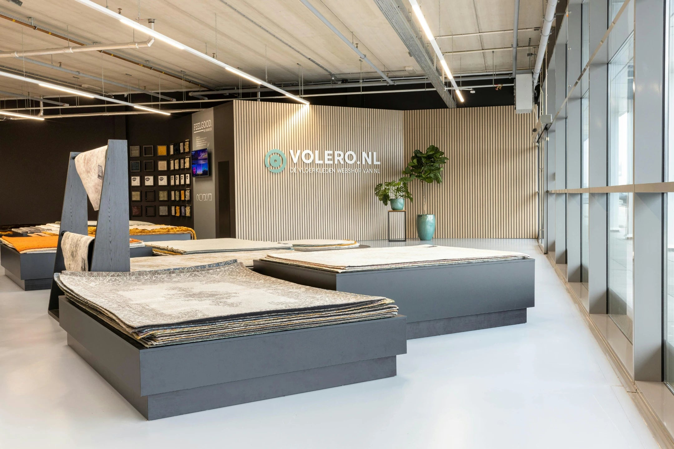 Rugs stacked on grey display platforms in front of the VOLERO.NL logo wall at the Amsterdam showroom